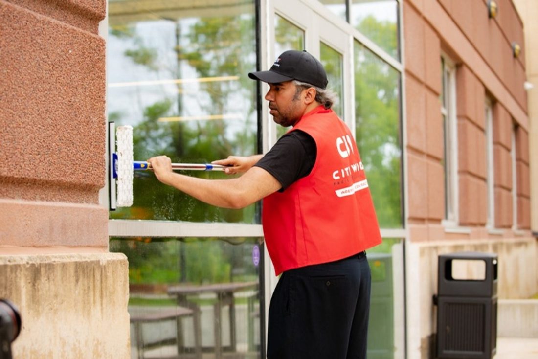Window cleaning vendor in a City Wide vest working on a commercial storefront